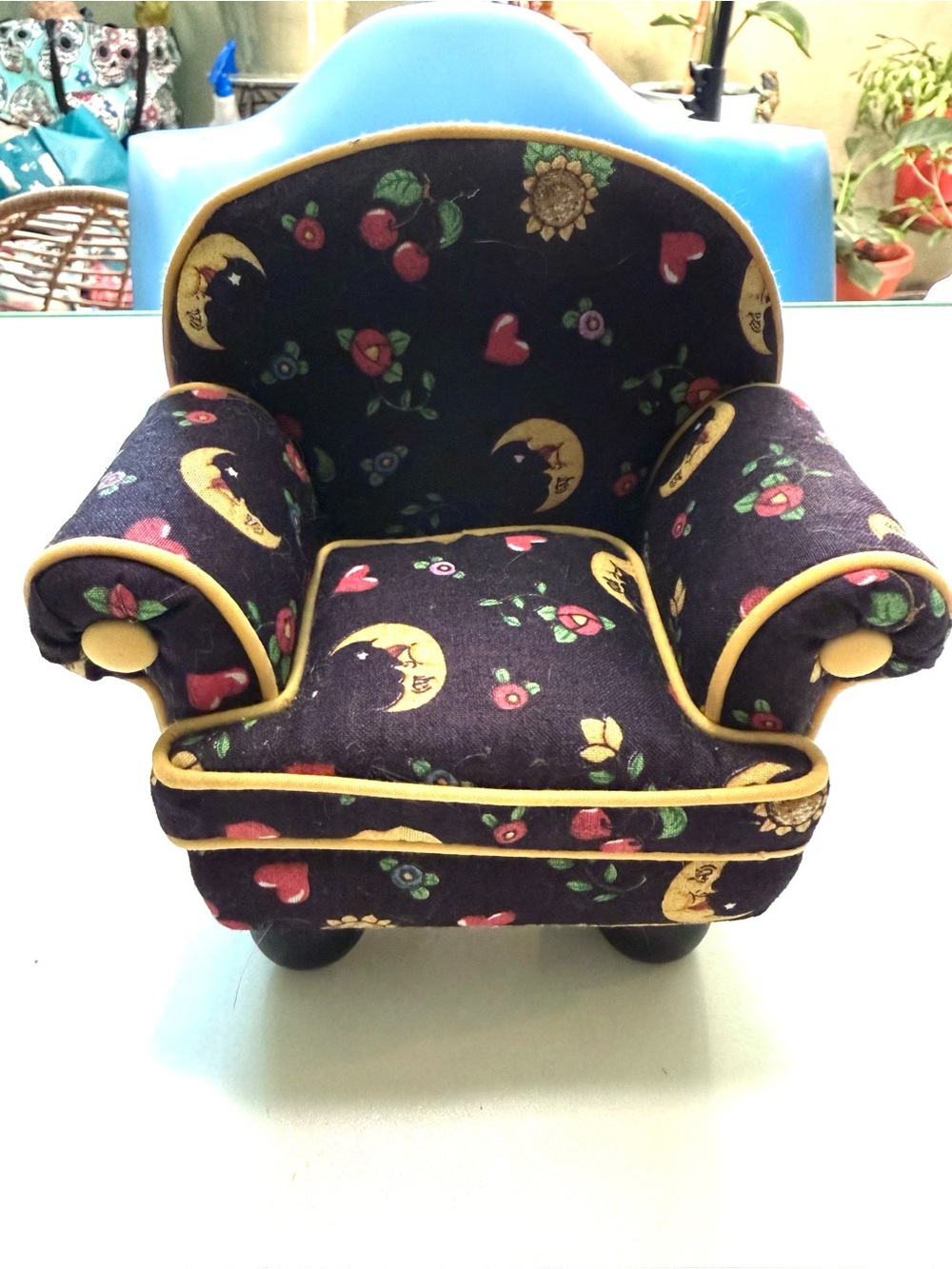 A miniature chair pincushion on dark fabric printed with cherries,moon & flowers